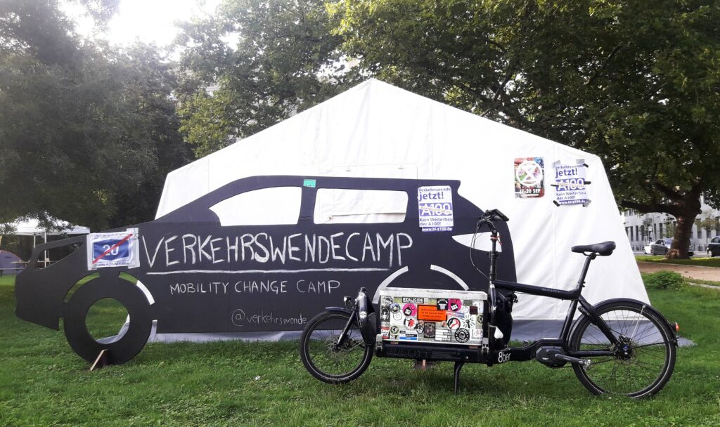 Lastenrad vor Zelt beim Verkehrswende Camp Berlin 2022 / Ausgeschnittenes Auto in schwarz mit Verkehrswendecamp Beschriftung